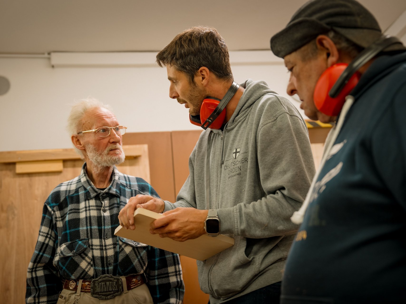 Zwei Bewohnende bekommen von einem Mitarbeitendem in der Werkstatt ein neues Projekt erklärt.