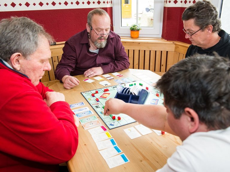 Vier Männer sitzen am Tisch und spielen Monopoly - es sind schon einige Häuser und Hotels aufgestellt