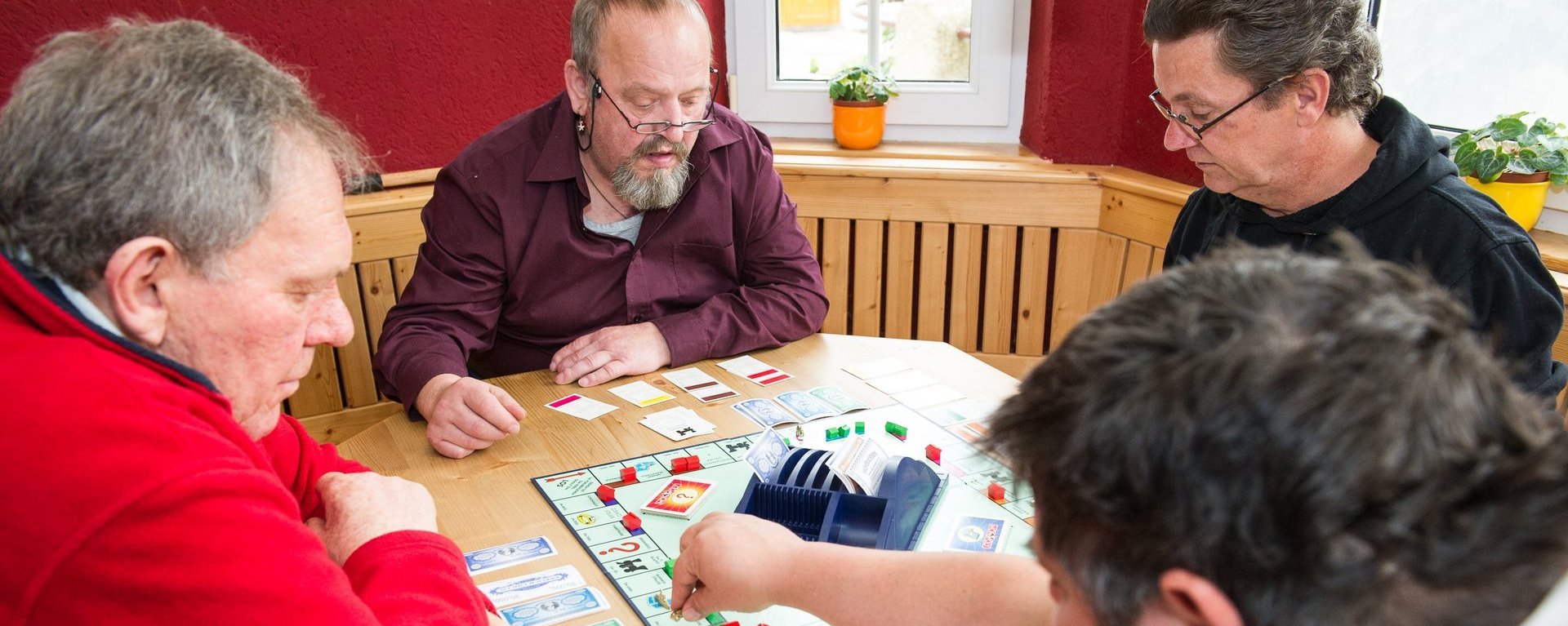 Vier Männer sitzen am Tisch und spielen Monopoly - es sind schon einige Häuser und Hotels aufgestellt