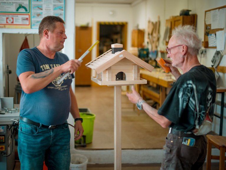 Ein Mitarbeitender und ein Bewohnender basteln gemeinsam in der Werkstatt der Einrichtung an einem Vogelhaus.