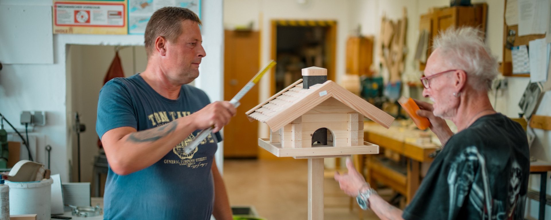 Ein Mitarbeitender und ein Bewohnender basteln gemeinsam in der Werkstatt der Einrichtung an einem Vogelhaus.