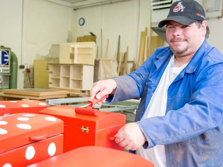 Mann in Arbeitskleidung lackiert mehrere Holztruhen in roter Farbe mit weissen Punkten