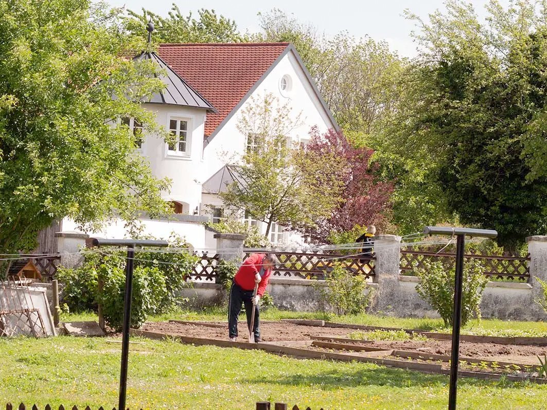 Blick zum Gemüsebeet: ein Mann hebt mit einem Spaten ein Loch aus