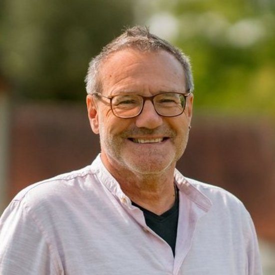 Ein Mitarbeitender steht in dem grünen Garten der Einrichtung.