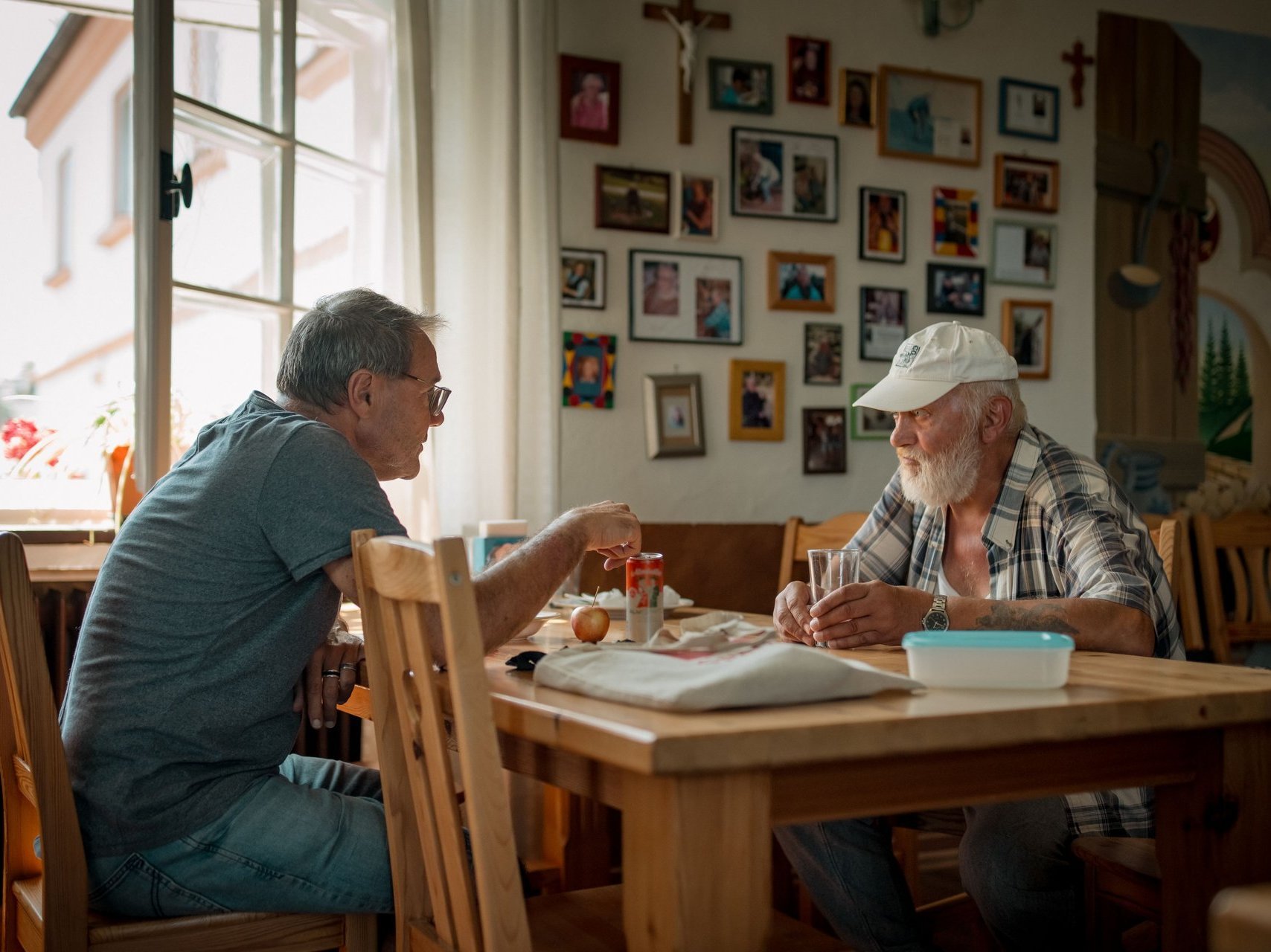 Mitarbeitender sitzt mit einem Bewohnendem am Essenstisch und erklärt etwas.