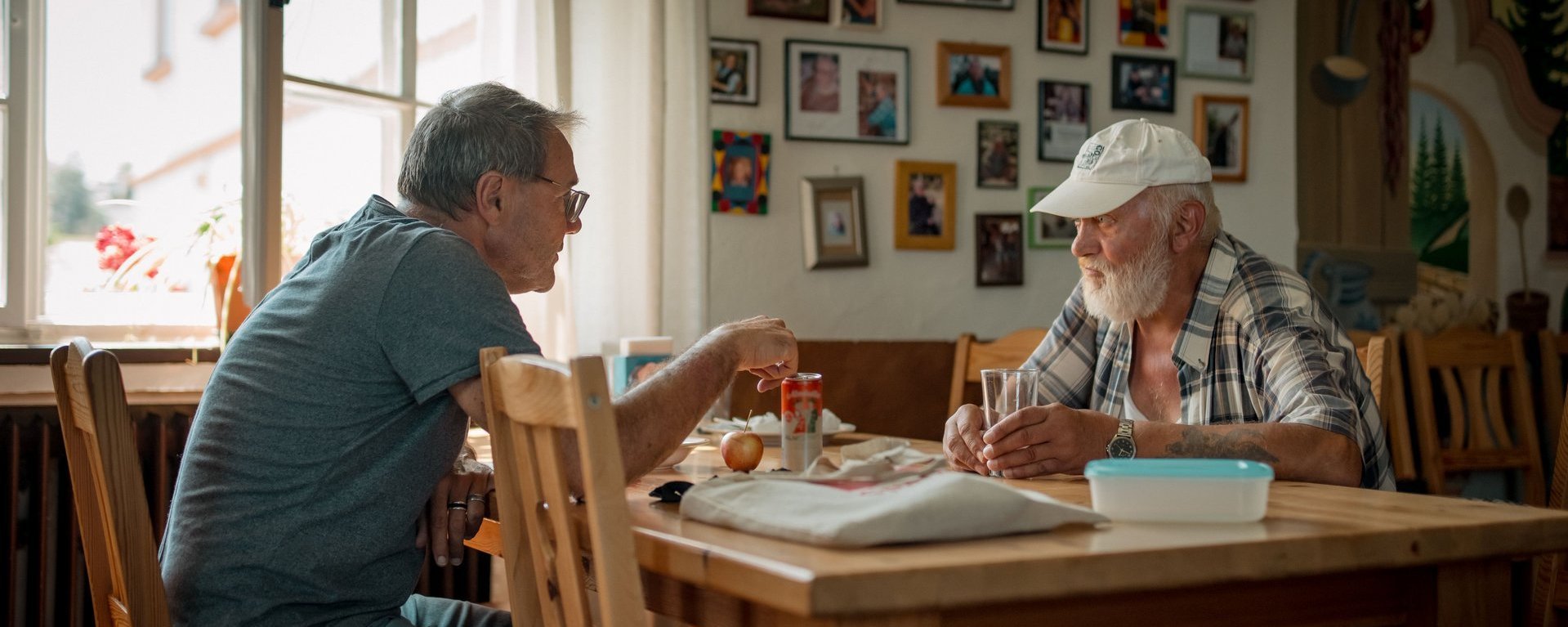 Mitarbeitender sitzt mit einem Bewohnendem am Essenstisch und erklärt etwas.