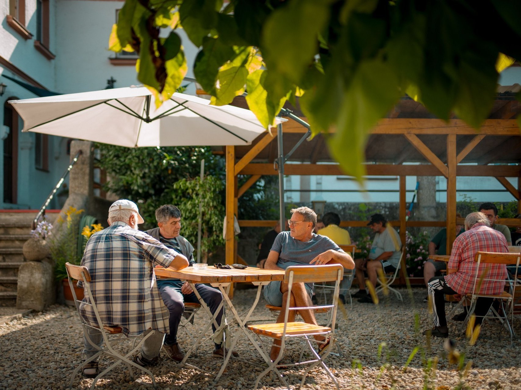 Männer sitzen draußen an Tischen unter Sonnenschirme und unterhalten sich.