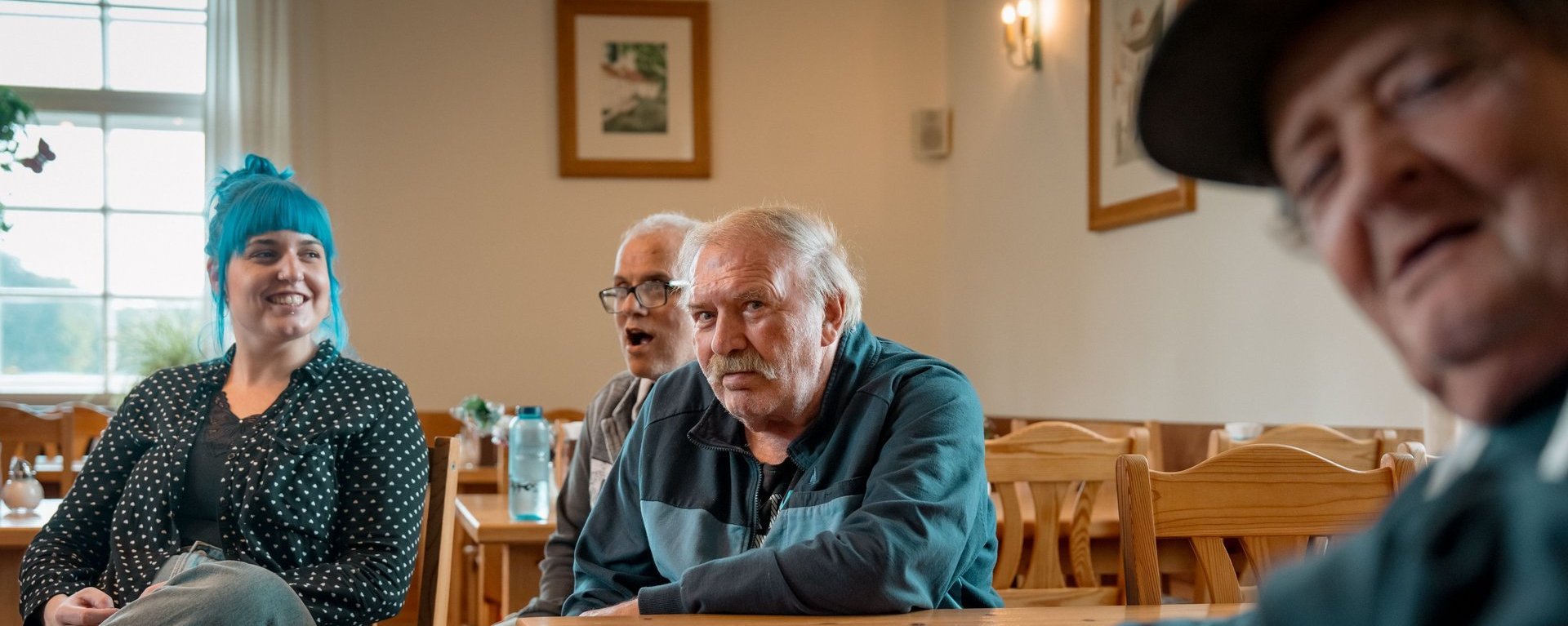 Eine Mitarbeitende und drei Bewohnende sitzen zusammen in einem Raum und Unterhalten sich.