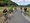 Eine Gruppe von Radfahrern auf einem asphaltierten Weg im Grünen. Eine Person sitzt auf einer Bank, deren Kopf durch einen riesigen grünen Brokkoli ersetzt wurde. Die anderen Radfahrer blicken in ihre Richtung.