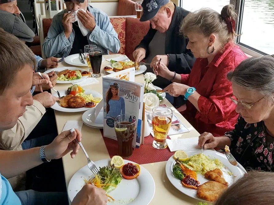 gemeinsames Mittagessen: Faruen und Männer sitzen zu Tisch - es gibt paniertes Schnitzel und Kartoffelsalat mit Beilagensalat