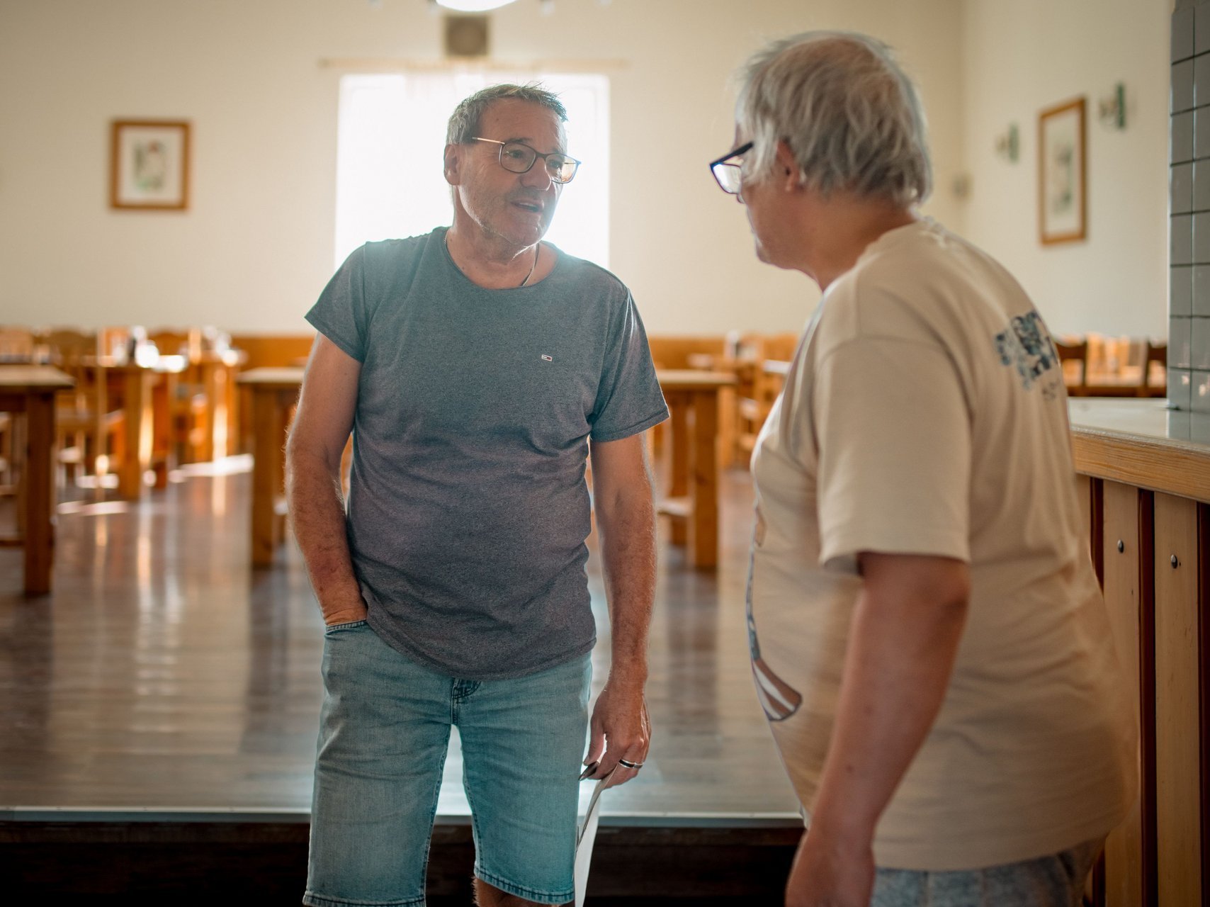 Zwei Männer stehen in einem Raum voller Tische und unterhalten sich.
