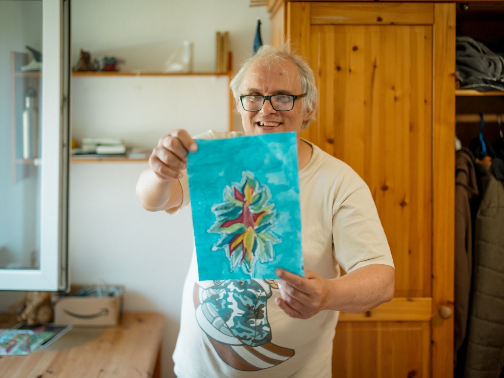 Ein Bewohnender zeigt stolz seine kreative Zeichnung in die Kamera und lacht dabei.
