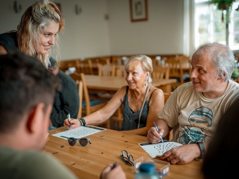 Bewohnende sitzen zusammen an einem Tisch und füllen mit viel Freude ein Kreuzworträtsel aus.