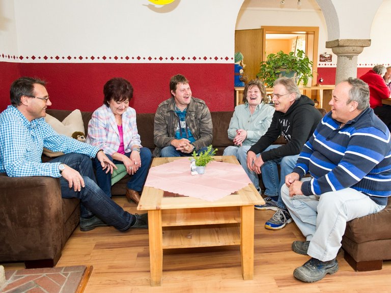 Frauen und Männer in lustiger Runde in einem Aufenthaltsraum lachen und unterhalten sich