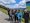 Eine Gruppe von sieben Wanderern posiert auf einem Bergpfad vor einer malerischen Landschaft mit grünen Hängen und blauem Himmel. Rechts steht eine Informationstafel mit einer Panoramakarte.
