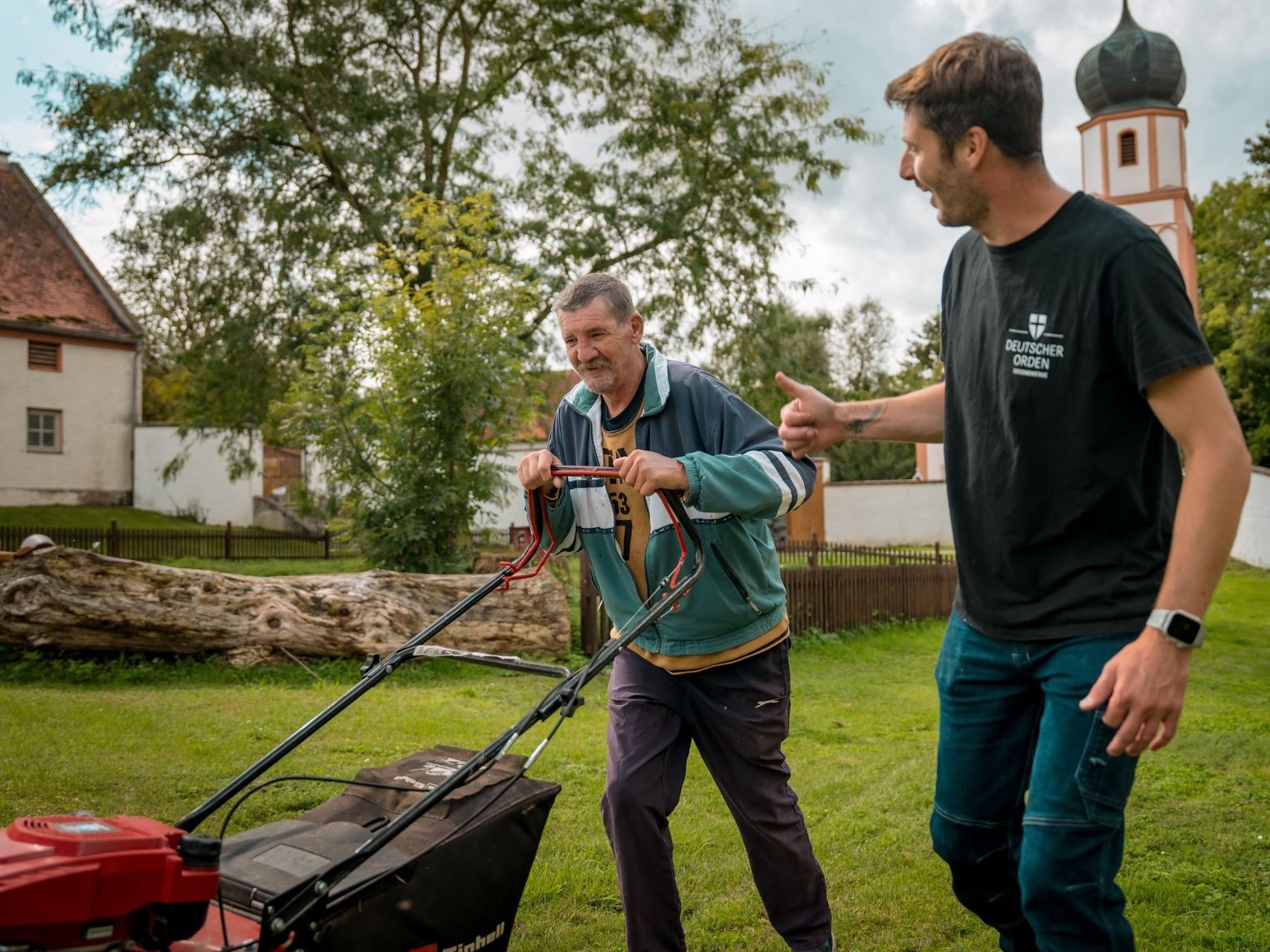 Zwei Männer mähen im großen Garten der Einrichtung den Rasen.