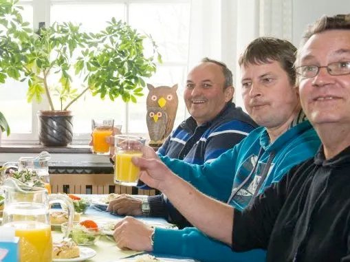 Hausbewohner beim Mittagessen prosten mit Orangensaft zur Kamera