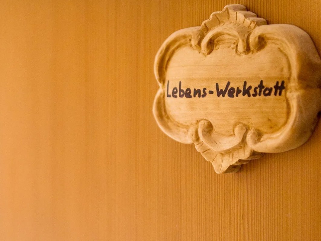 Blick auf eine halb geöffnete Tür mit dem auf verzierten Holz geschnitzten Wort "Lebens-Werkstatt"